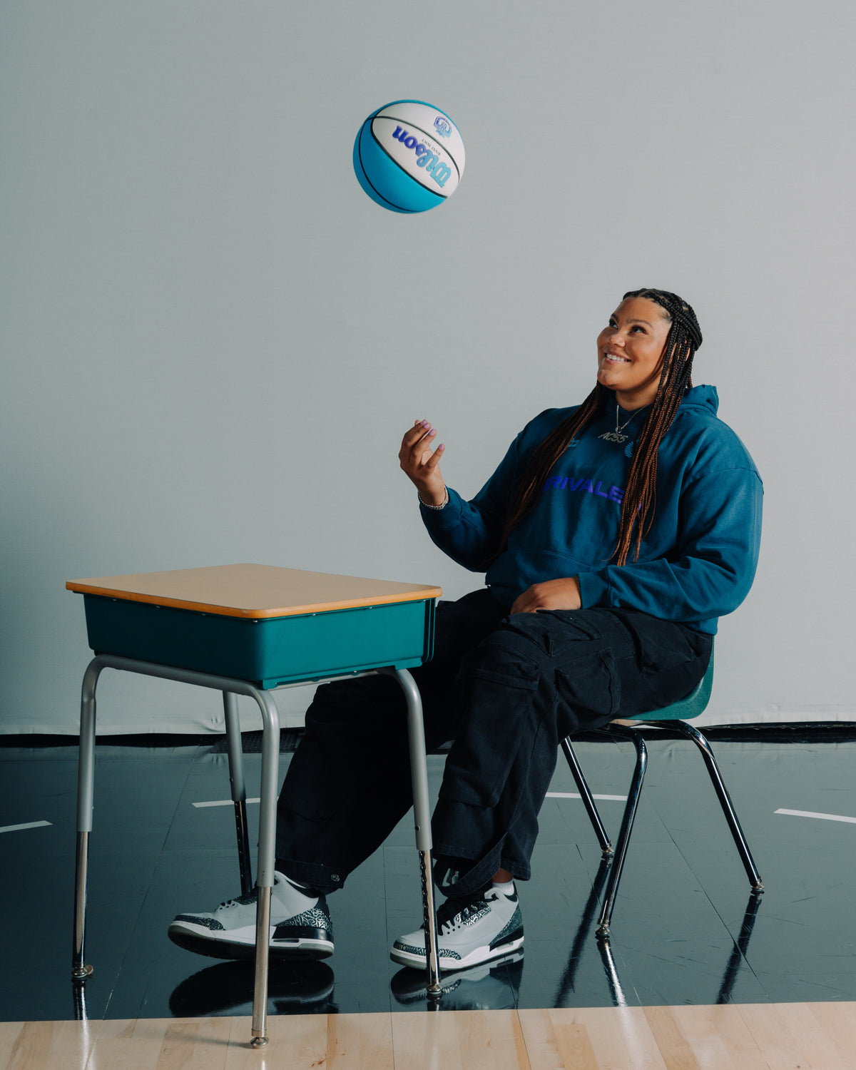 Audi Crooks sitting on a chair with a basketball above them, in front of a gray wall.